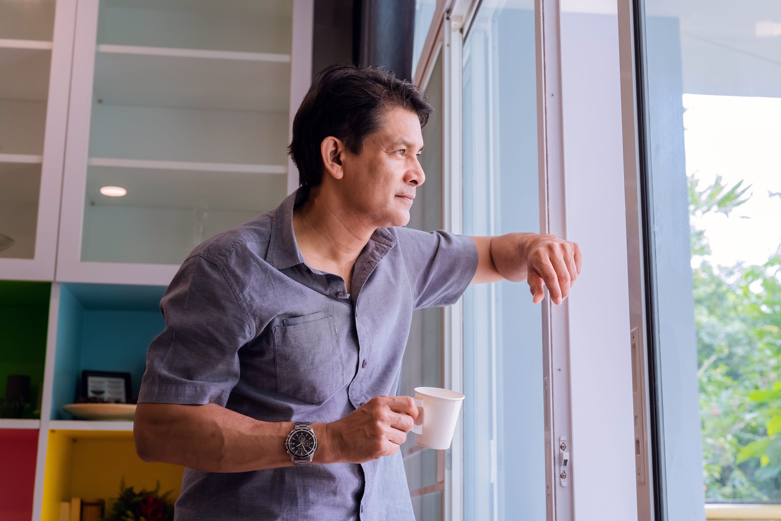 Middle-aged Asian man looking through a window, sipping coffee and using ideas Middle-aged Asian man looking through a window, sipping coffee and using ideas