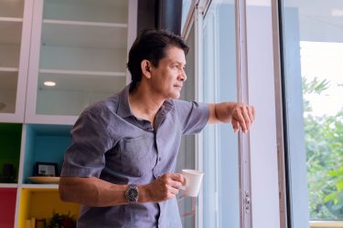 Middle-aged Asian man looking through a window, sipping coffee and using ideas Middle-aged Asian man looking through a window, sipping coffee and using ideas